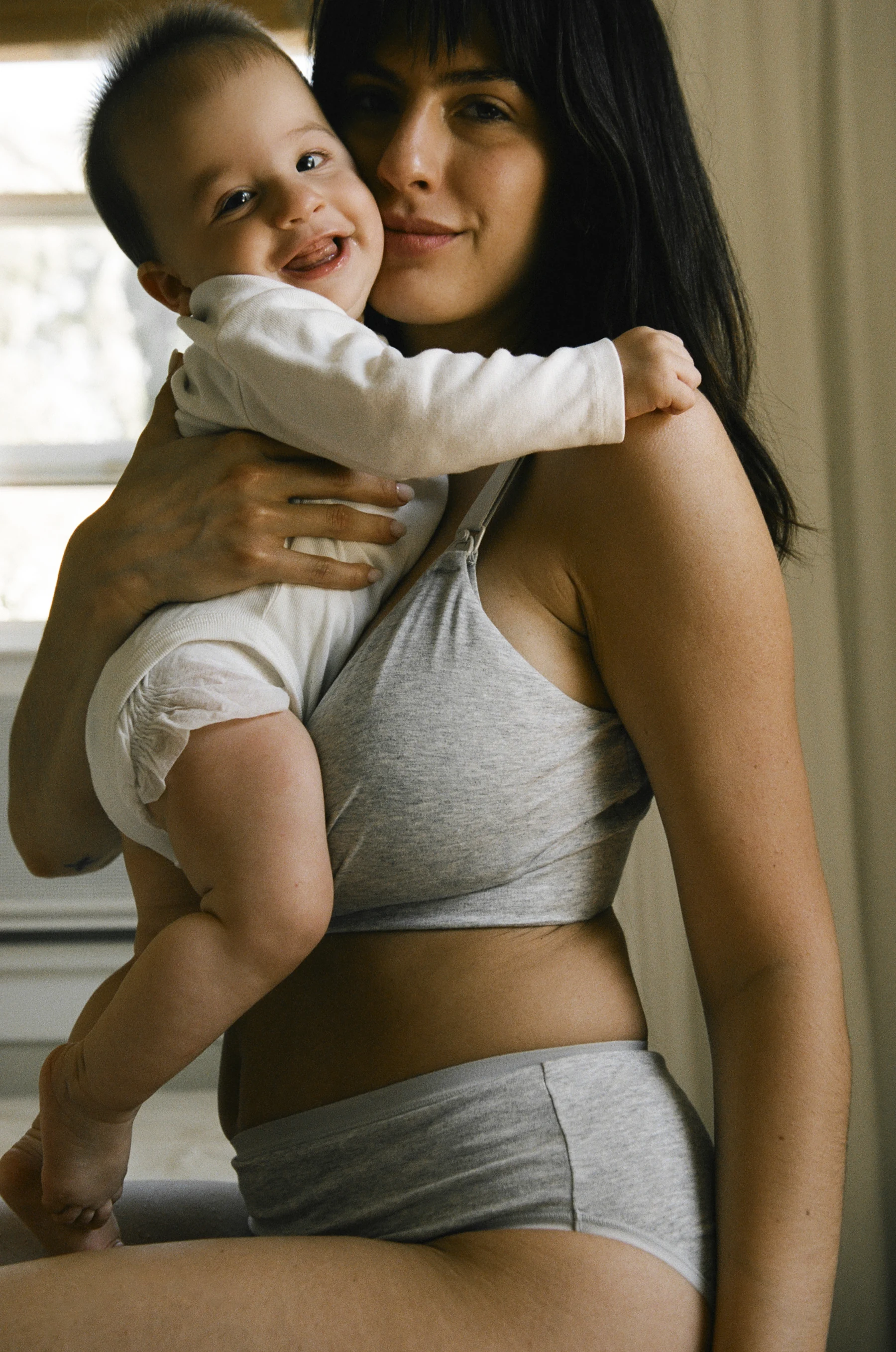 Mother holding her smiling baby while wearing Kindred Bravely nursing apparel