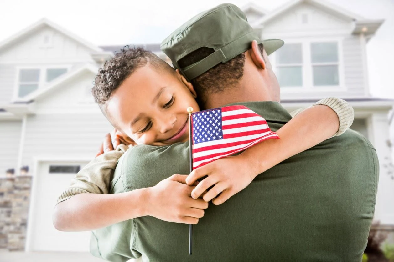 Military service member embracing a child outside a home